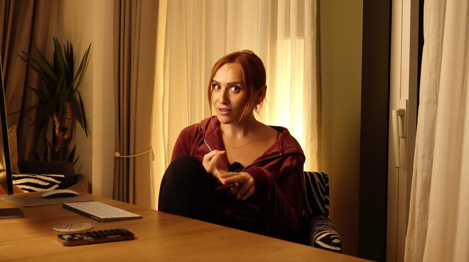 Chloe mid-sentence at her desk in a warm, lamp-lit room, gesturing as she talks to camera.